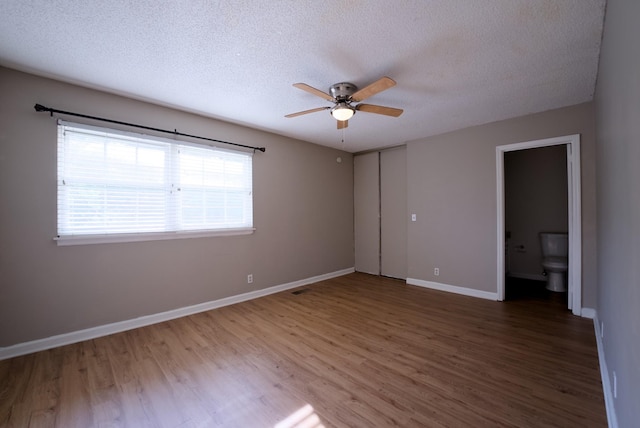 unfurnished bedroom featuring ceiling fan, ensuite bathroom, hardwood / wood-style floors, and a textured ceiling