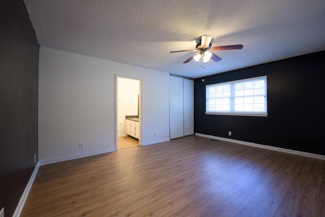 unfurnished bedroom with ceiling fan, connected bathroom, hardwood / wood-style floors, and a textured ceiling