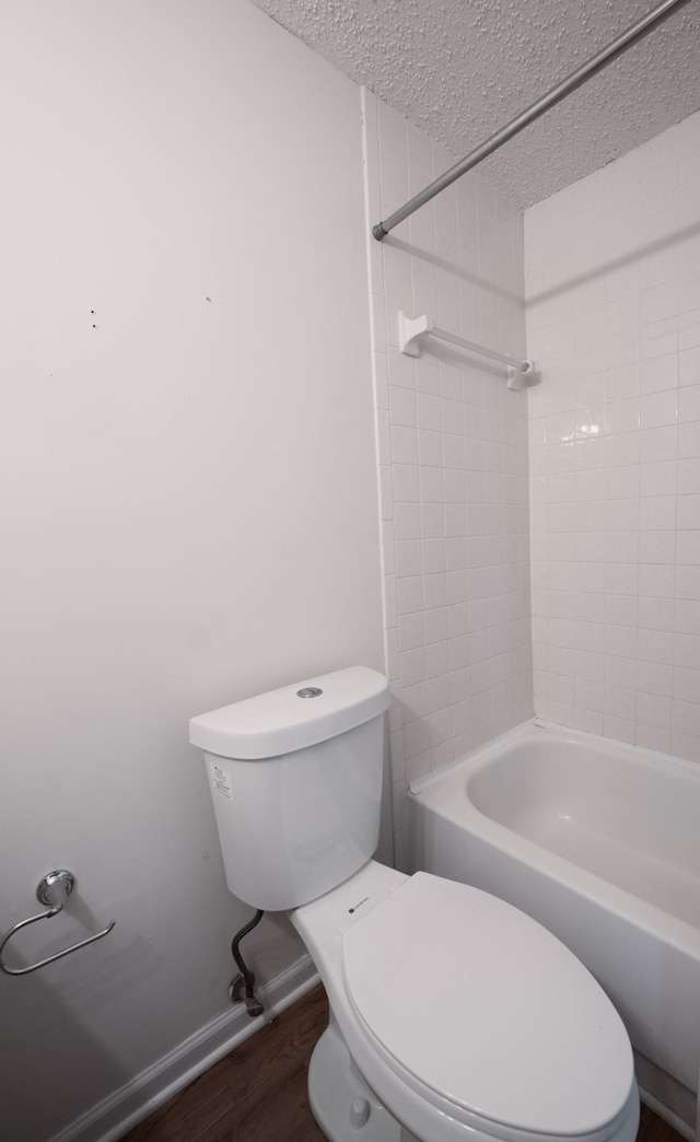 bathroom featuring wood-type flooring, shower / washtub combination, toilet, and a textured ceiling