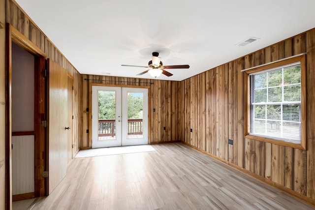 spare room with light wood-type flooring, french doors, wood walls, and ceiling fan