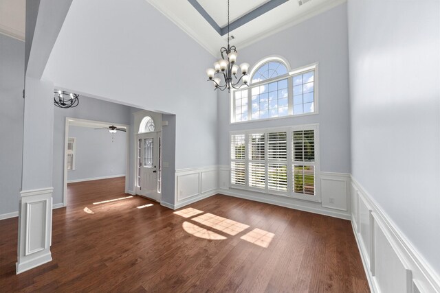 interior space with dark hardwood / wood-style floors, ceiling fan with notable chandelier, crown molding, and a high ceiling