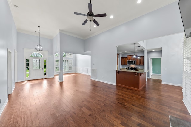 unfurnished living room with ornamental molding, wood-type flooring, ceiling fan with notable chandelier, and a towering ceiling