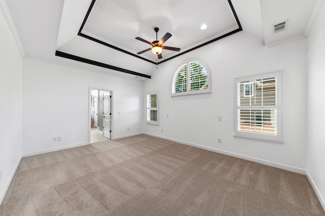 empty room featuring a tray ceiling, light carpet, crown molding, and ceiling fan