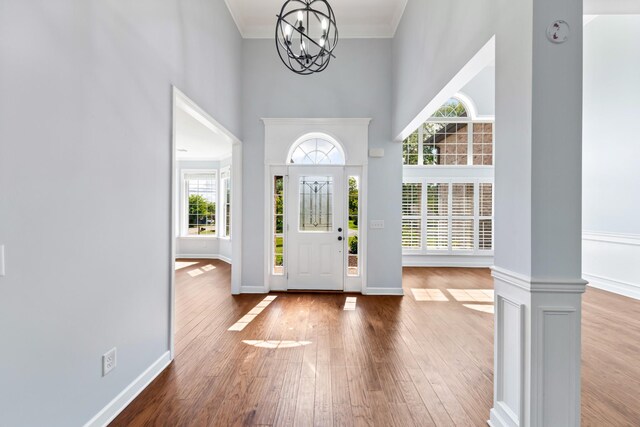 entrance foyer featuring hardwood / wood-style floors, crown molding, ornate columns, a chandelier, and a towering ceiling