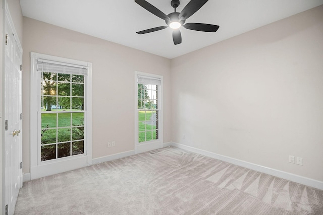 spare room with a ceiling fan, light colored carpet, and baseboards