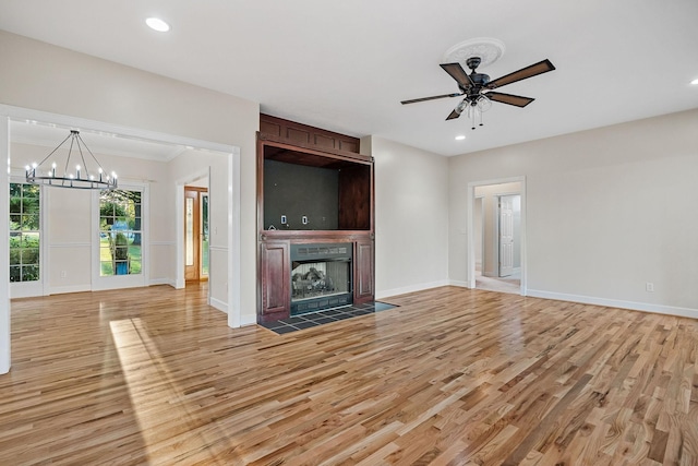 unfurnished living room with recessed lighting, ceiling fan with notable chandelier, a fireplace with flush hearth, baseboards, and light wood-style floors