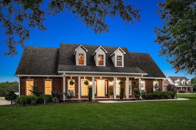 cape cod home featuring covered porch, a front lawn, a shingled roof, and brick siding