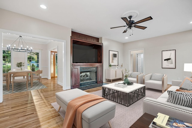 living room featuring recessed lighting, ceiling fan with notable chandelier, a fireplace, baseboards, and light wood-style floors