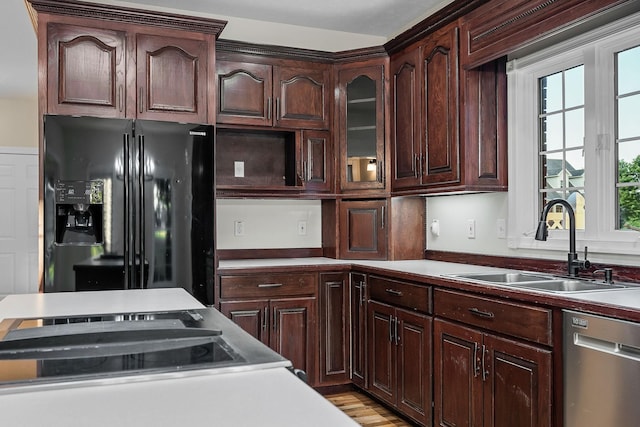 kitchen with a sink, light countertops, stainless steel dishwasher, black refrigerator with ice dispenser, and glass insert cabinets