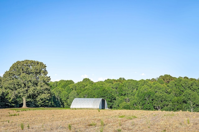 view of yard with a rural view, an outdoor structure, and a view of trees