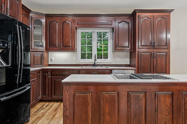 kitchen featuring light wood finished floors, glass insert cabinets, light countertops, black appliances, and a sink