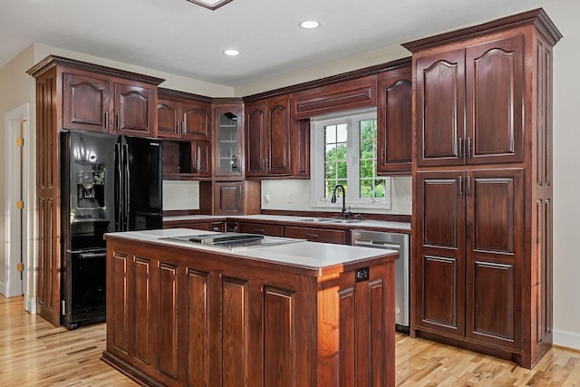 kitchen featuring light countertops, a center island, dishwasher, black refrigerator with ice dispenser, and glass insert cabinets