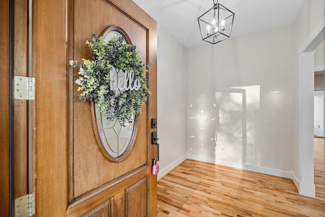 entryway featuring baseboards, light wood-type flooring, and an inviting chandelier