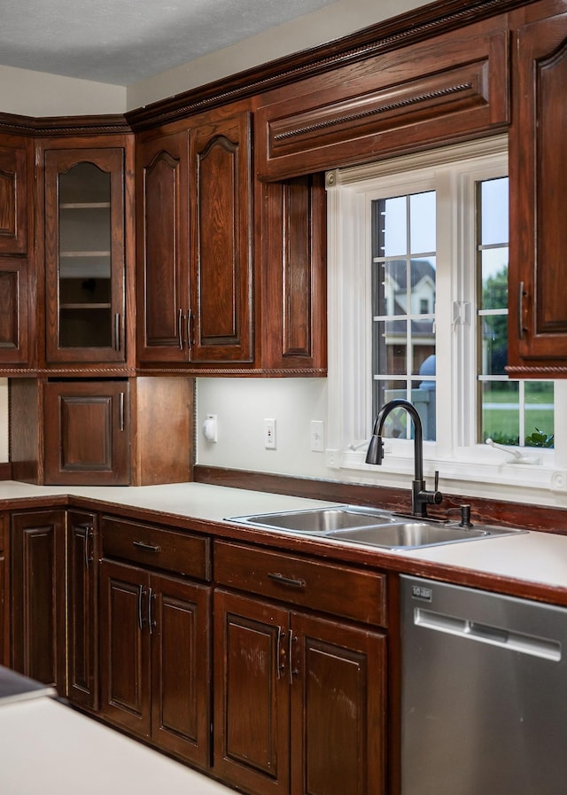 kitchen featuring stainless steel dishwasher, glass insert cabinets, a sink, and dark brown cabinetry