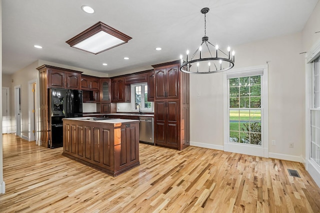 kitchen featuring visible vents, light countertops, hanging light fixtures, a kitchen island, and black appliances