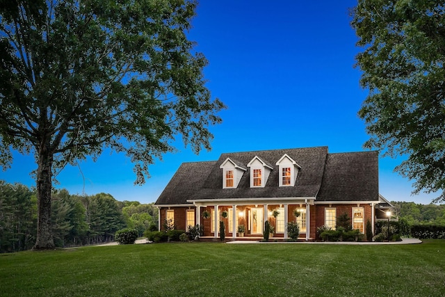 cape cod-style house featuring brick siding, a porch, and a front yard