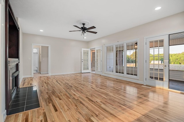 unfurnished living room featuring french doors, light wood finished floors, recessed lighting, a fireplace with flush hearth, and baseboards