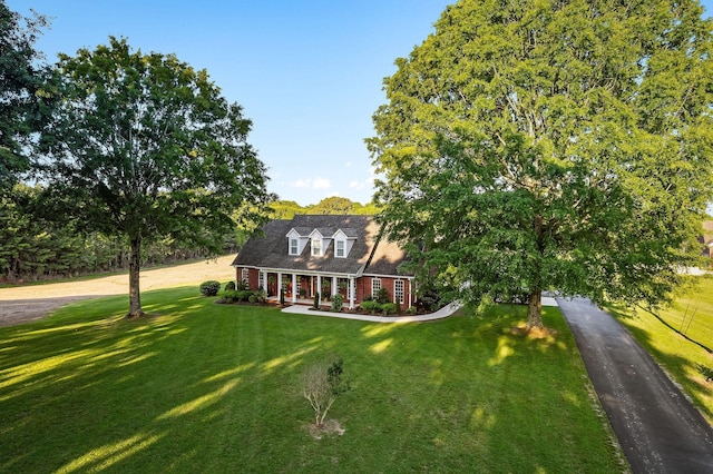 cape cod home featuring aphalt driveway, a front yard, covered porch, and brick siding