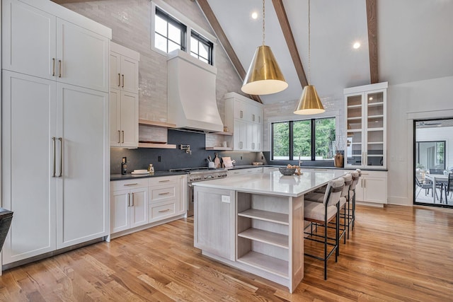 kitchen with high end stainless steel range, white cabinetry, a center island, light hardwood / wood-style flooring, and beamed ceiling