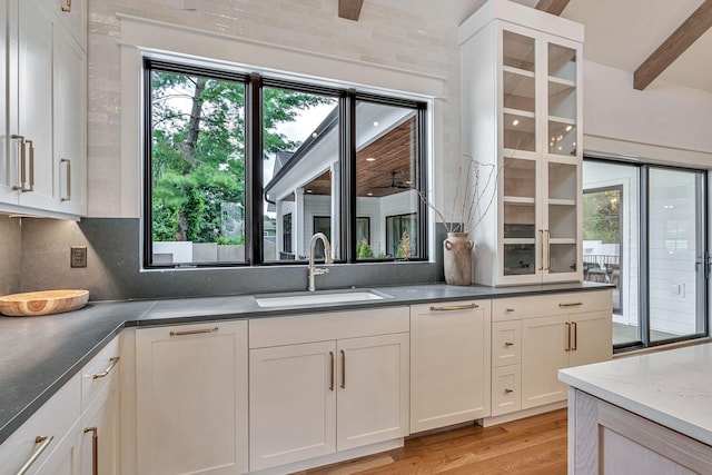 kitchen with sink, light hardwood / wood-style flooring, beam ceiling, white cabinets, and decorative backsplash