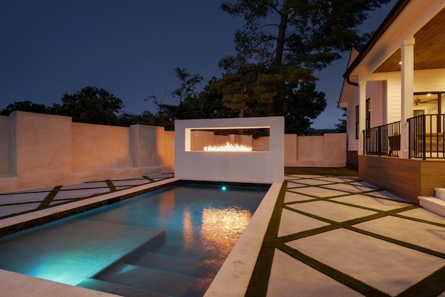 pool at night with exterior fireplace and a patio area