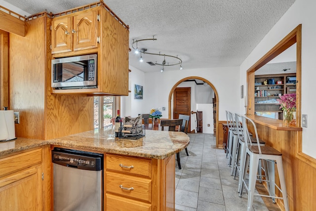 kitchen with light tile patterned flooring, rail lighting, a textured ceiling, light stone countertops, and appliances with stainless steel finishes