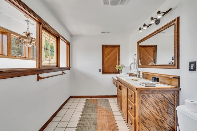 bathroom with a notable chandelier, toilet, tile patterned flooring, and dual bowl vanity