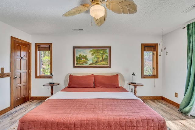 bedroom with a textured ceiling, wood-type flooring, and ceiling fan