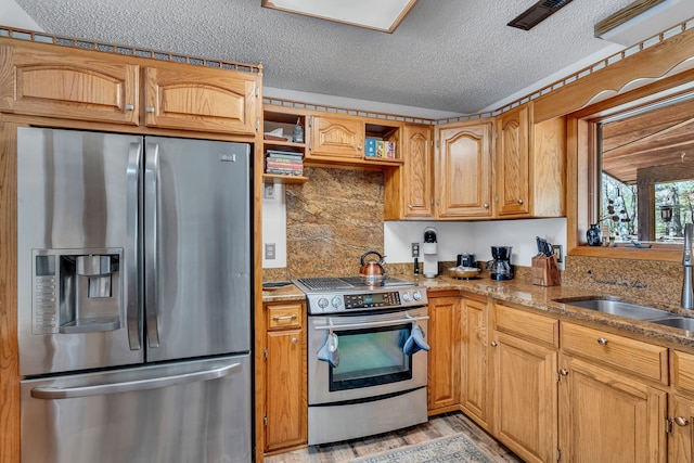 kitchen featuring stainless steel appliances, sink, light stone countertops, light hardwood / wood-style flooring, and a textured ceiling