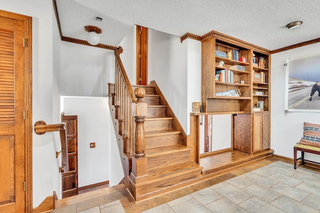 stairway with a textured ceiling, light tile patterned floors, and crown molding