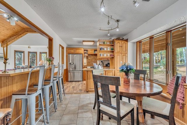 dining space with lofted ceiling with beams, a textured ceiling, light tile patterned floors, and track lighting