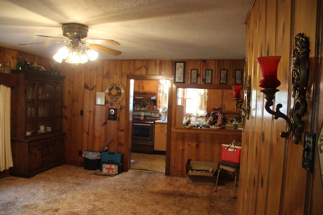 kitchen featuring ceiling fan, stainless steel electric stove, wooden walls, carpet, and a textured ceiling