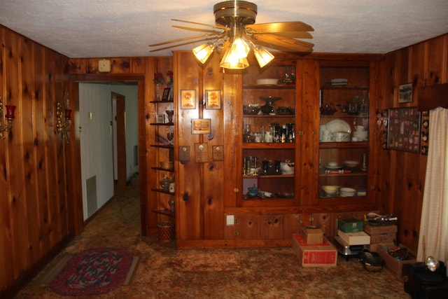 interior space featuring ceiling fan, a textured ceiling, and wooden walls