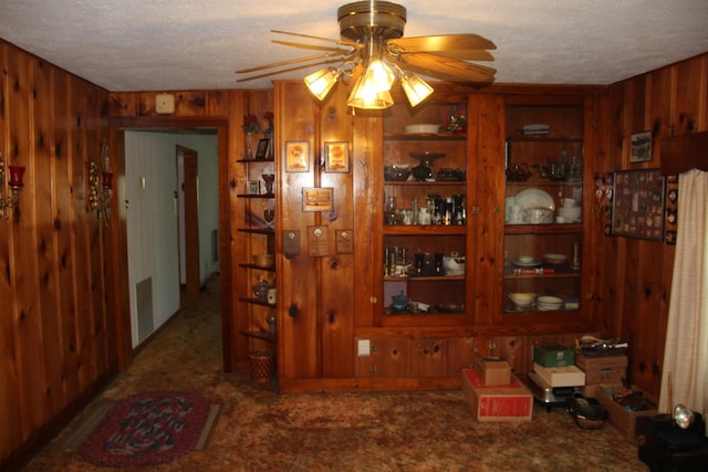 carpeted dining space with ceiling fan, a textured ceiling, and wooden walls