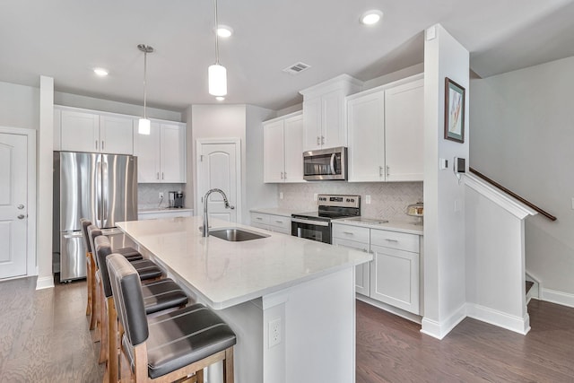 kitchen featuring a center island with sink, pendant lighting, sink, white cabinetry, and appliances with stainless steel finishes