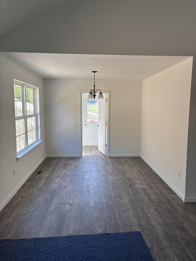 spare room with dark wood-type flooring, a healthy amount of sunlight, a notable chandelier, and baseboards