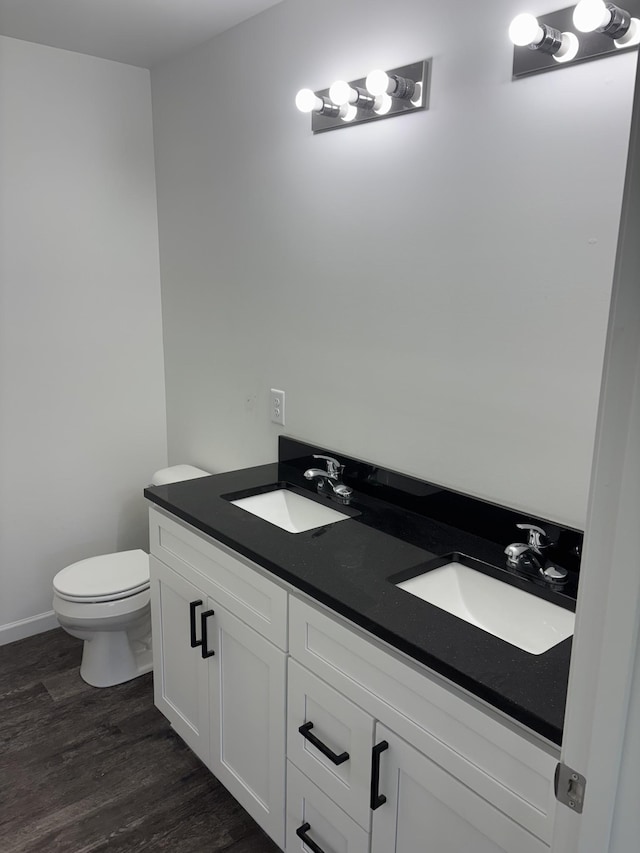 bathroom featuring toilet, wood finished floors, double vanity, and a sink