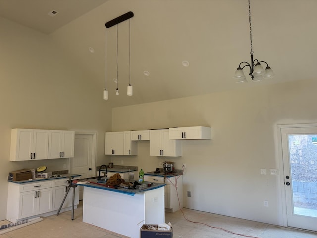 kitchen with an inviting chandelier, white cabinets, a towering ceiling, decorative light fixtures, and a kitchen island