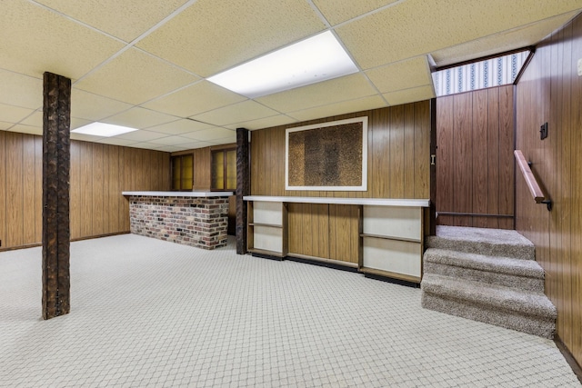 basement with wood walls, indoor bar, and a drop ceiling