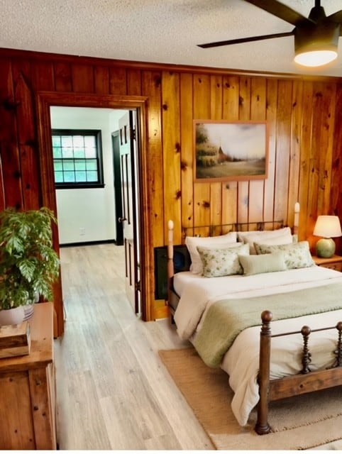 bedroom with a textured ceiling, ceiling fan, and wooden walls