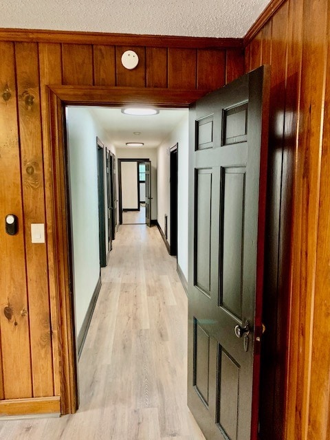 hall featuring wood walls, light hardwood / wood-style floors, and a textured ceiling