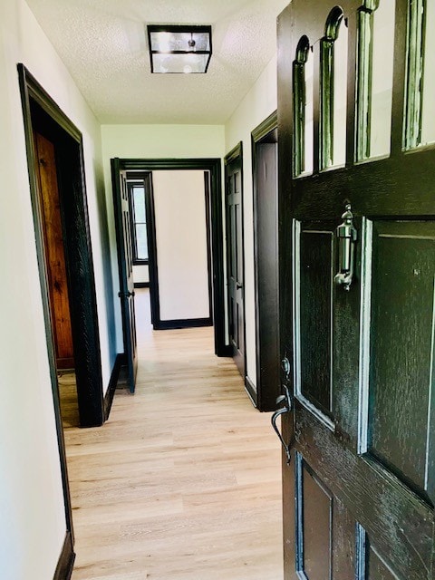 corridor with a textured ceiling and light hardwood / wood-style flooring