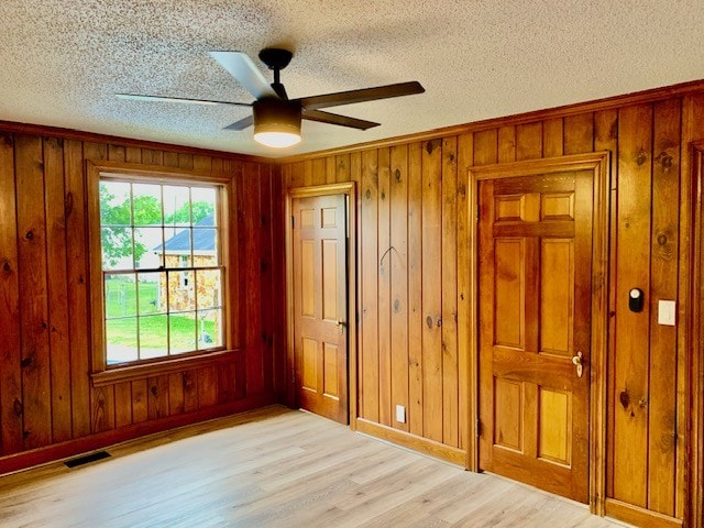 unfurnished bedroom featuring ceiling fan, wood walls, a textured ceiling, and light hardwood / wood-style flooring