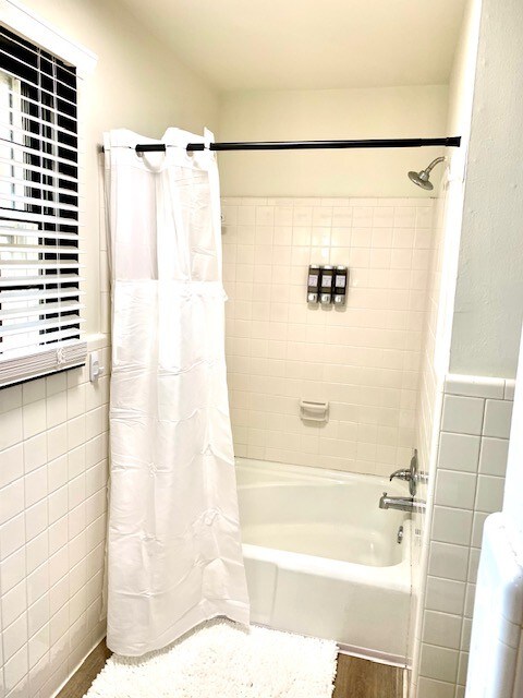 bathroom with hardwood / wood-style flooring, tile walls, and shower / tub combo with curtain