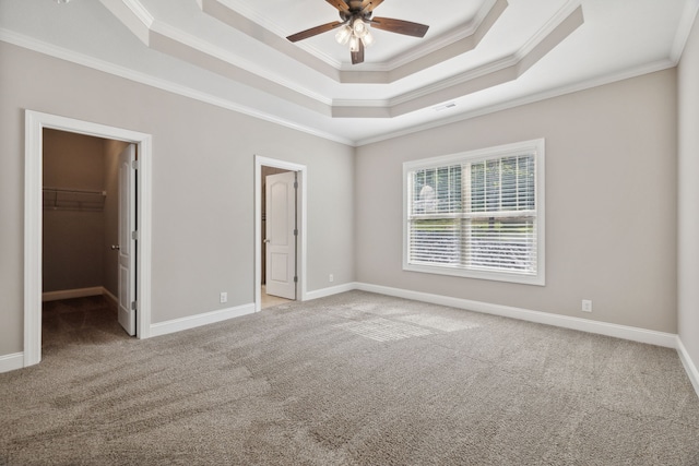 unfurnished bedroom featuring a raised ceiling, a walk in closet, and ornamental molding