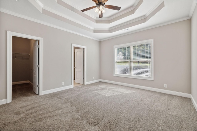 unfurnished bedroom featuring a raised ceiling, crown molding, a spacious closet, and light carpet