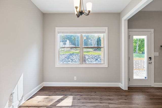 spare room featuring dark wood-type flooring, a chandelier, and plenty of natural light