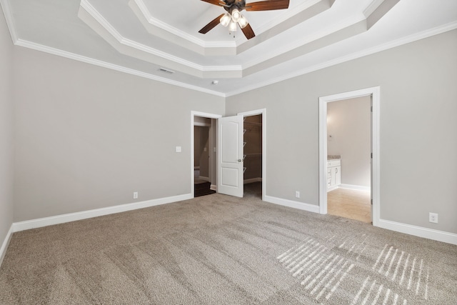 unfurnished bedroom with ensuite bathroom, a raised ceiling, carpet floors, and ornamental molding