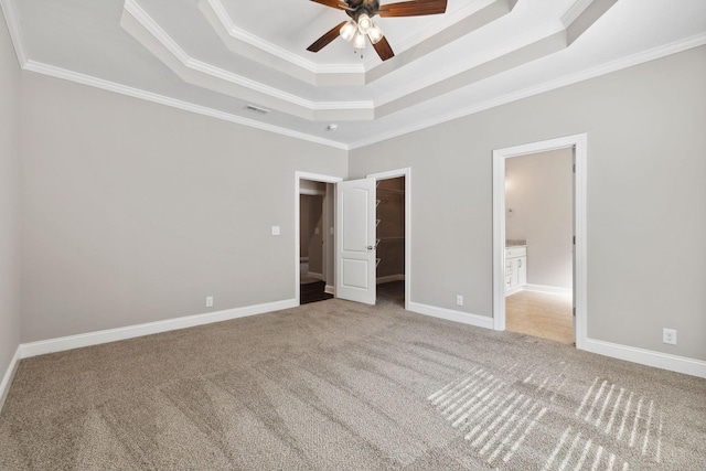 unfurnished bedroom featuring a tray ceiling, ornamental molding, a spacious closet, light colored carpet, and a closet