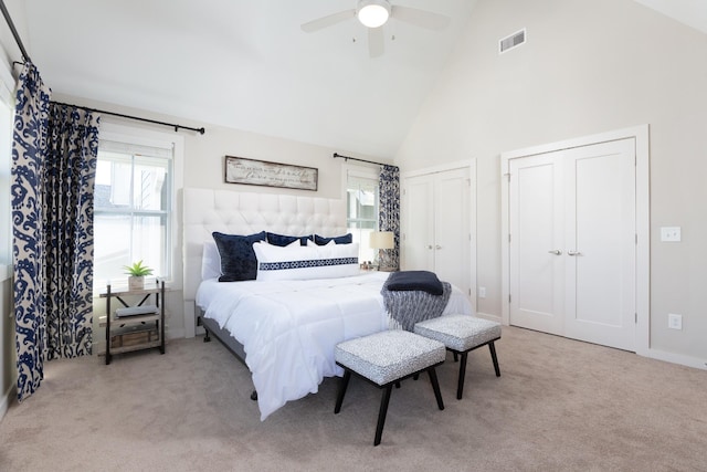 bedroom featuring multiple closets, ceiling fan, light carpet, and high vaulted ceiling